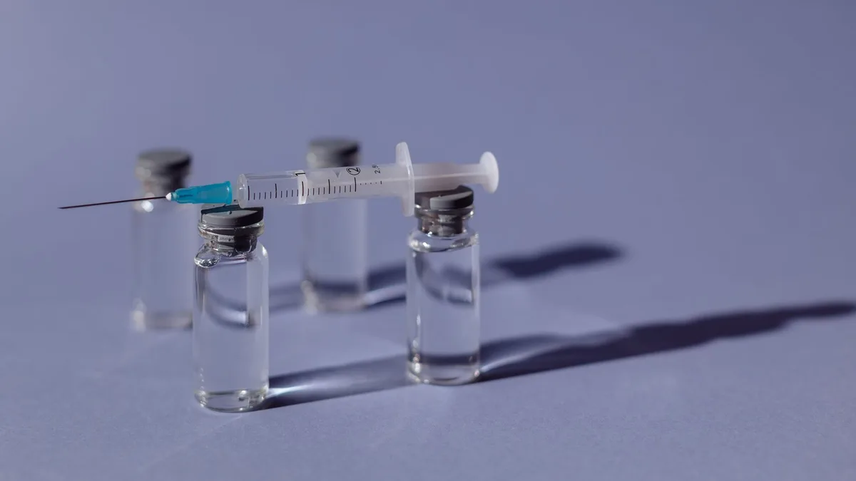 A syringe balanced on vaccine vials with a purple backdrop, representing medical treatment.