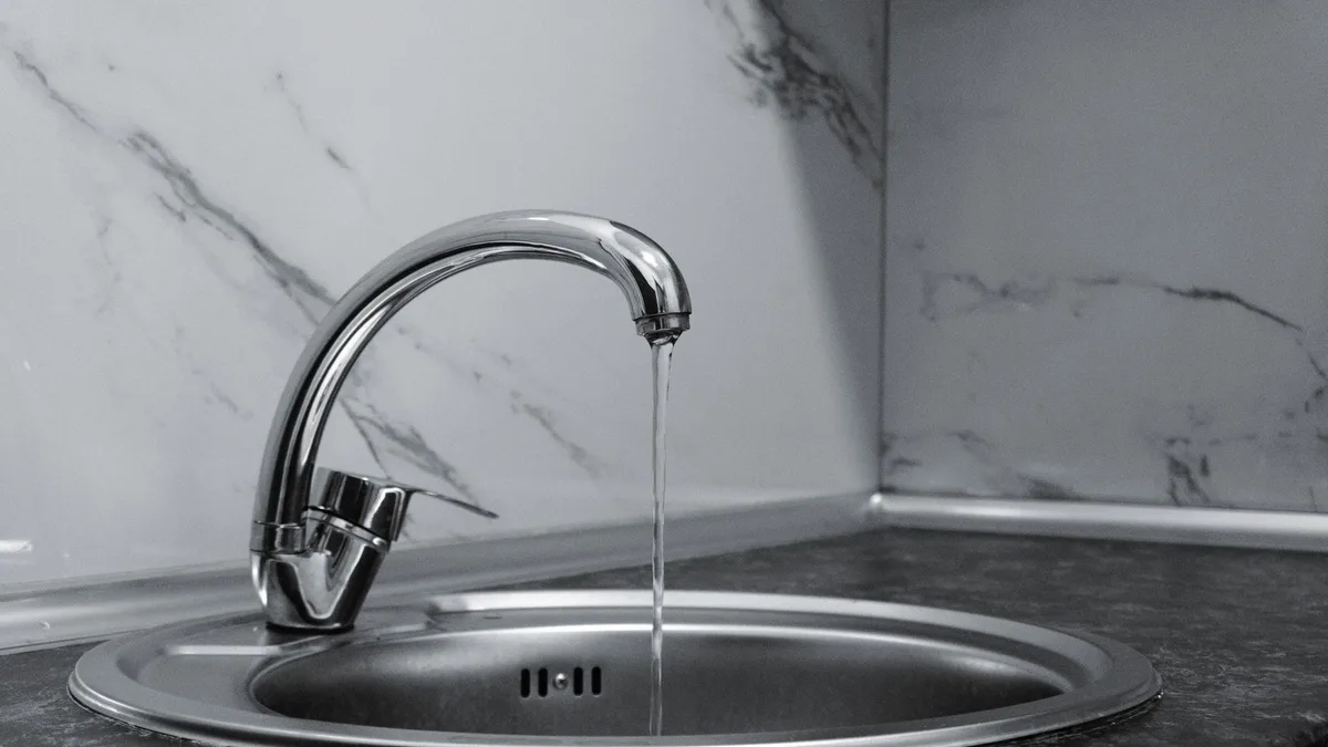 Chrome faucet with running water in a modern kitchen with marble countertop.