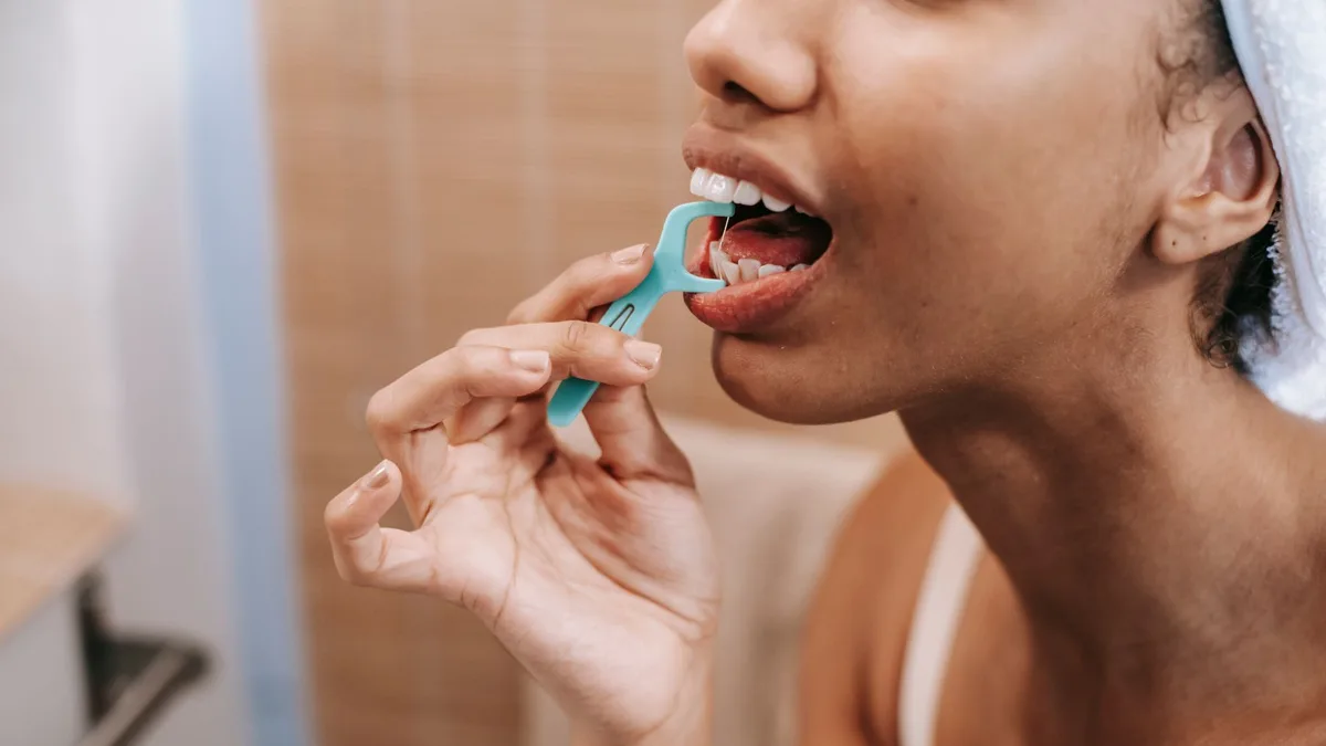 Crop ethnic female doing oral procedure with dental flosser in morning at home