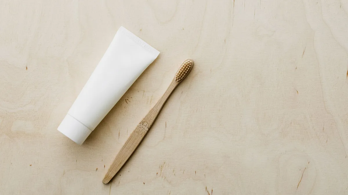 Overhead view of white mockup toothpaste tube and light brown bamboo toothbrush placed on wooden copy space surface