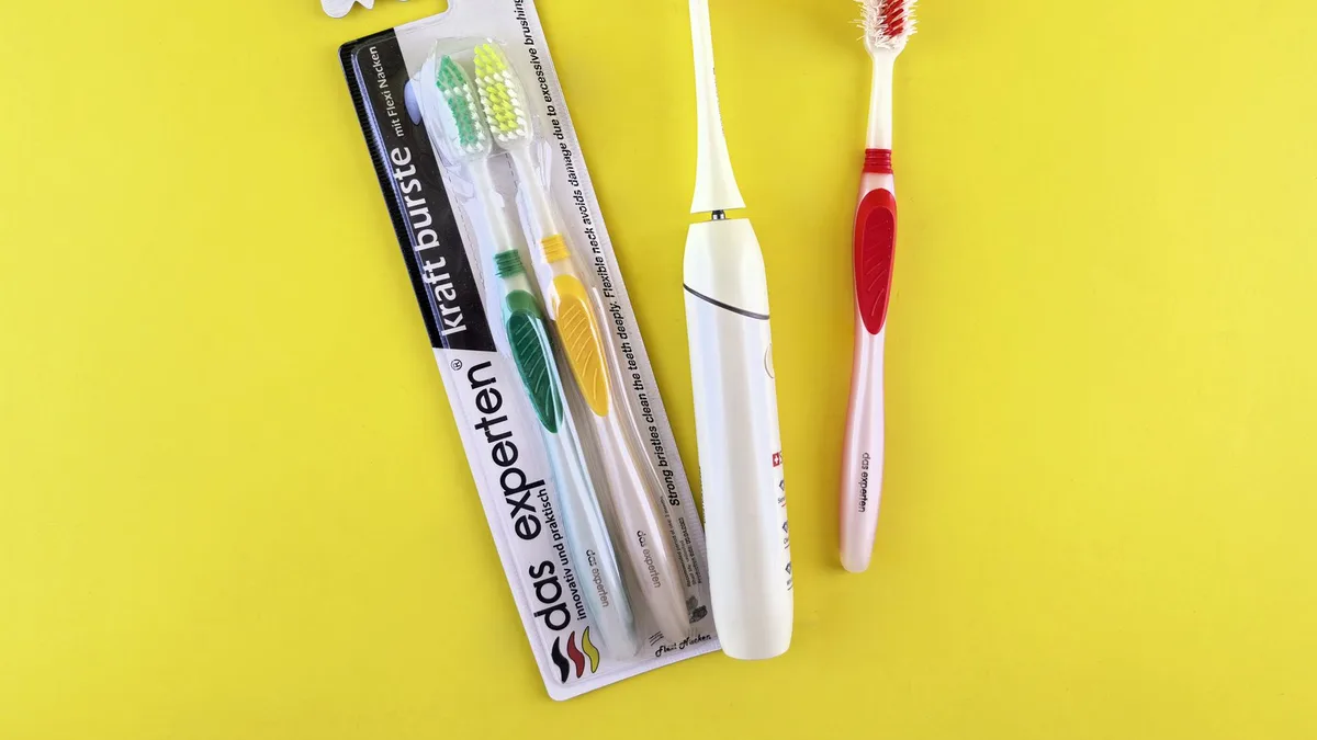 Flat lay of manual and electric toothbrushes with vibrant yellow background.